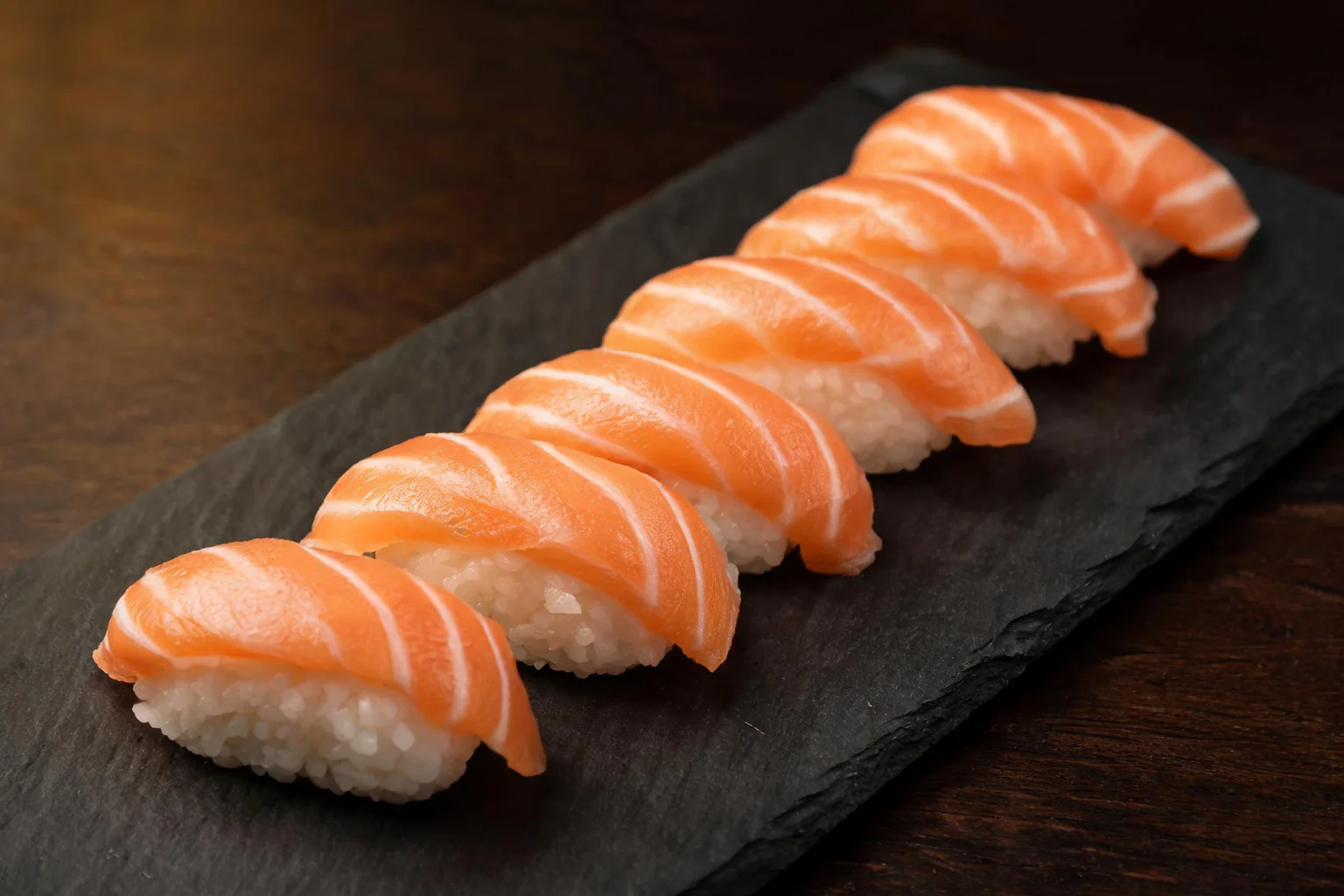 Salmon nigiri lined up on a black slate (illustration).