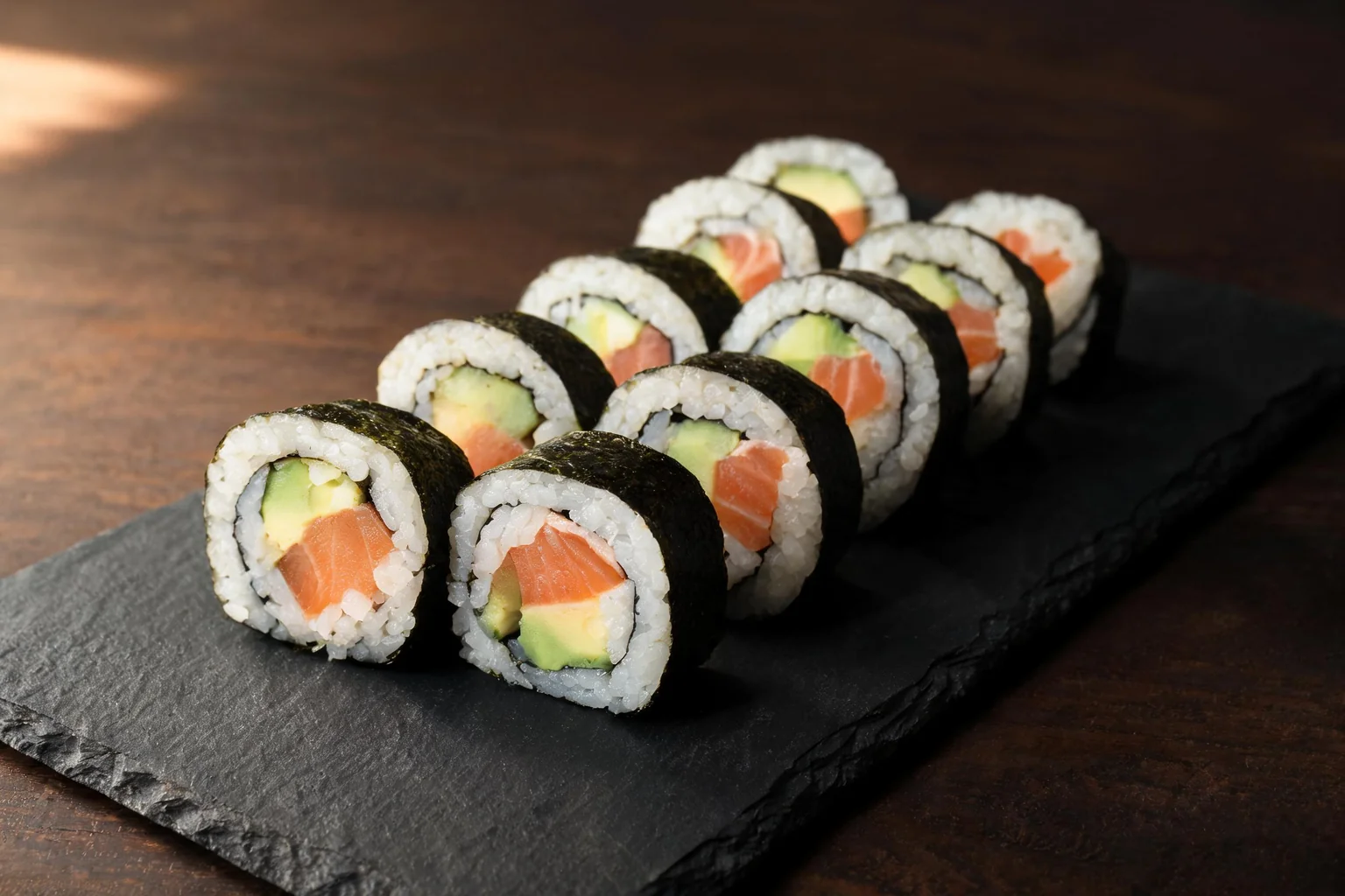 Salmon and avocado maki on a black slate (illustration).
