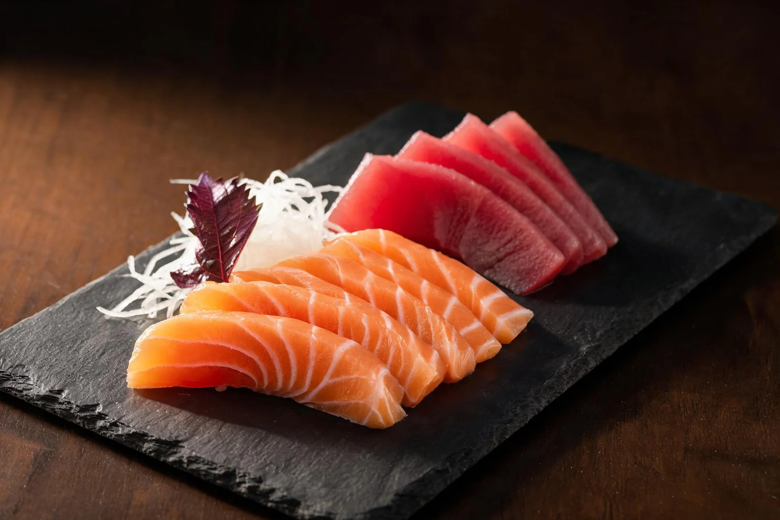 Slices of salmon and tuna, shredded radish and a shiso leaf on a slate (illustration).