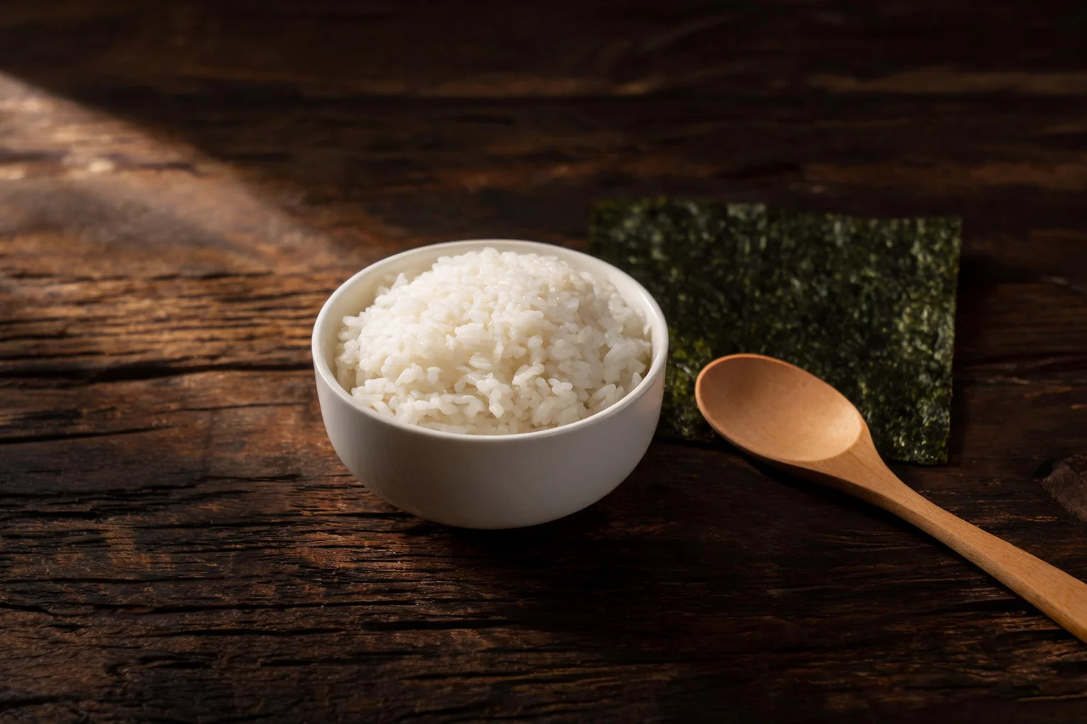 A bowl of white rice, a sheet of nori and a wooden spoon. (illustration)