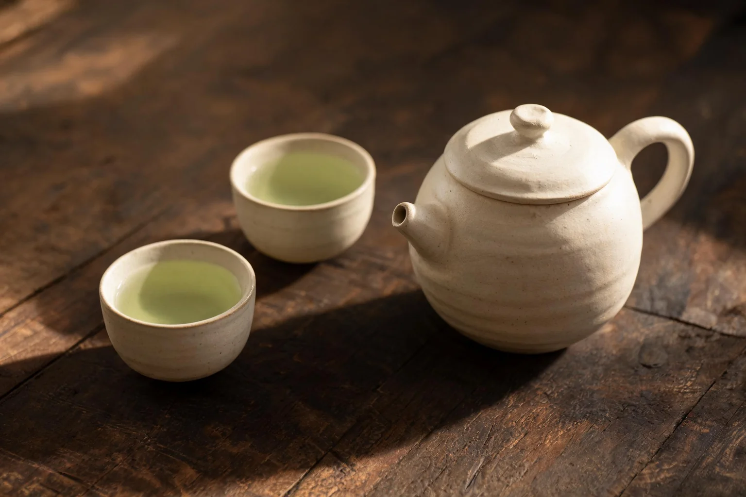 A ceramic teapot and two small cups of green tea. (illustration)